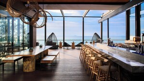 A modern bar area with a long counter, bar stools, and wicker hanging lights. - Renaissance Pattaya Resort & Spa (Sattahip)