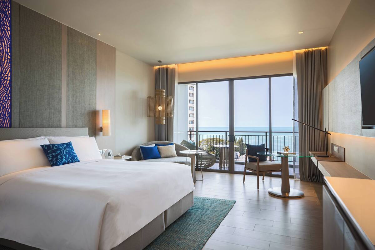 A modern hotel room with a large bed, a balcony with a view, a small table, and a TV.