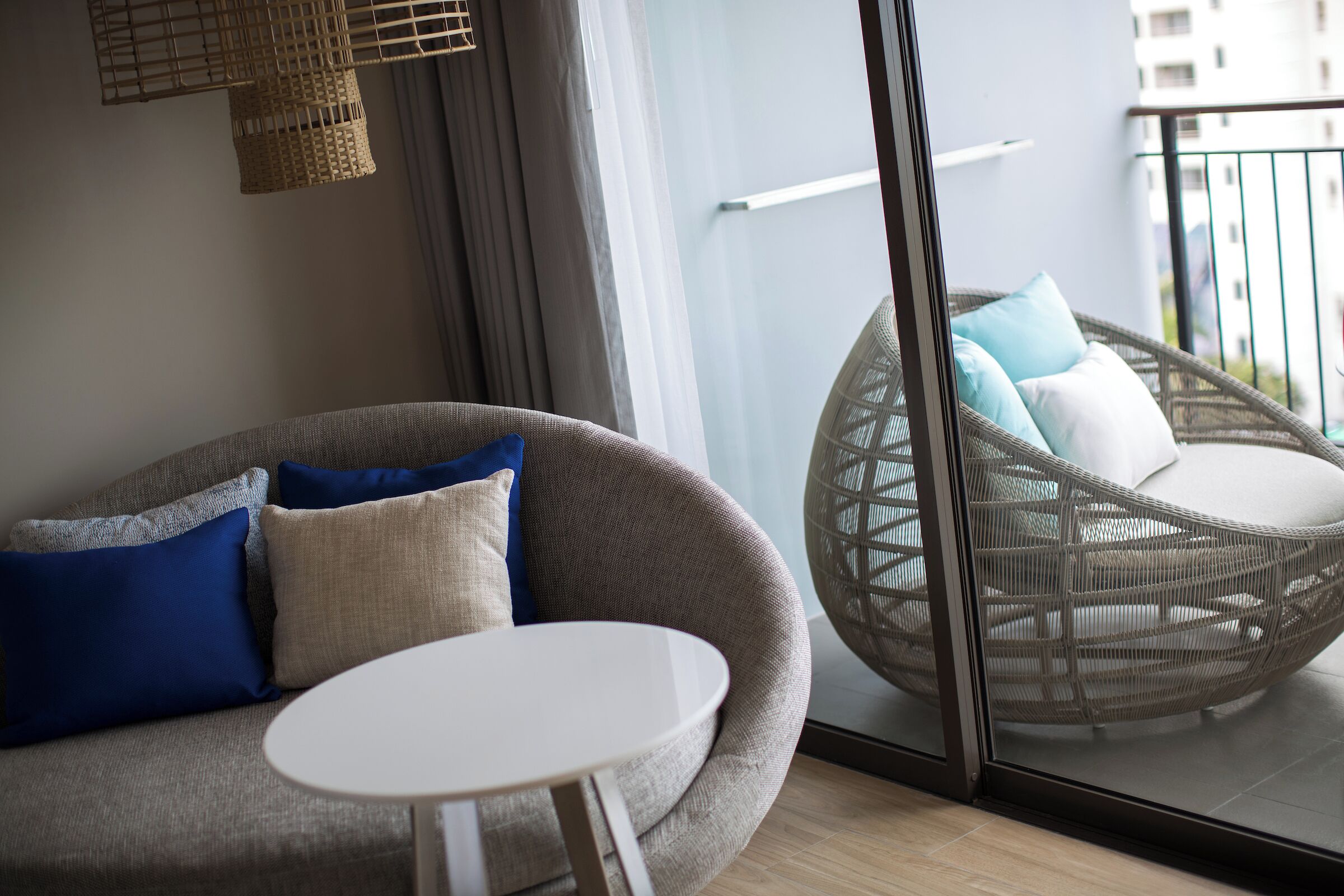 Un salón moderno con un sofá gris, una mesa redonda blanca y una silla de mimbre con cojines.