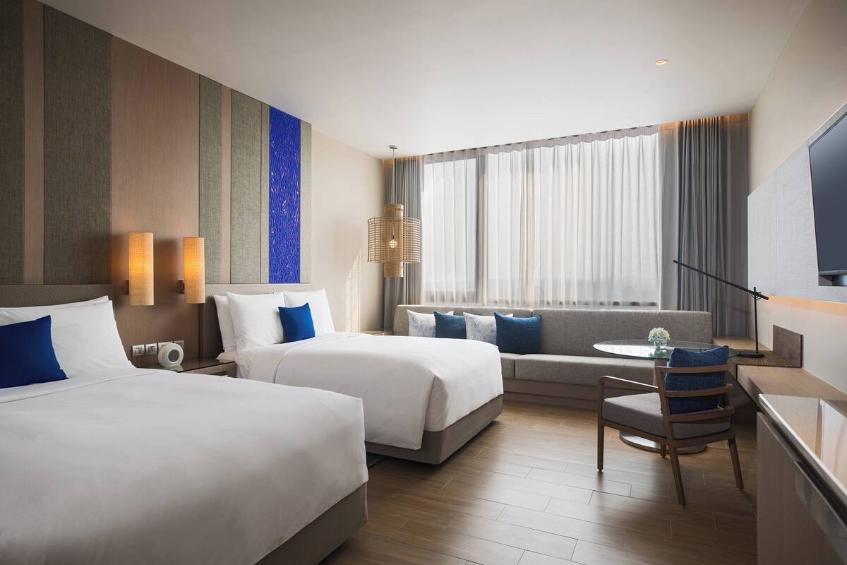 A hotel room with two beds, a sofa, a small table, and a TV.