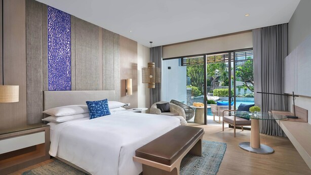 Habitación de hotel moderna con una cama grande, un banco, una mesa de vidrio y vistas al exterior.