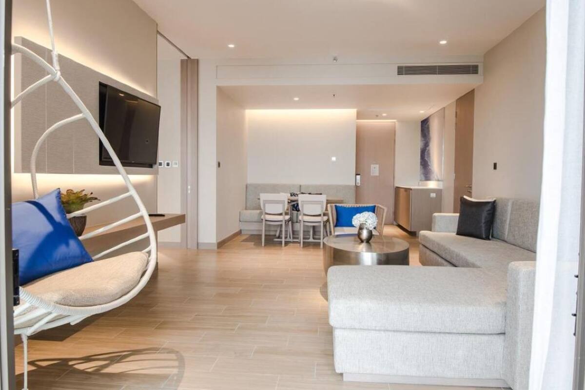 A modern living room with a sofa, a coffee table, a hanging chair, a TV mounted on the wall, and a dining area with chairs and a table.