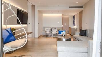 A modern living room with a sofa, a coffee table, a hanging chair, a TV mounted on the wall, and a dining area with chairs and a table.