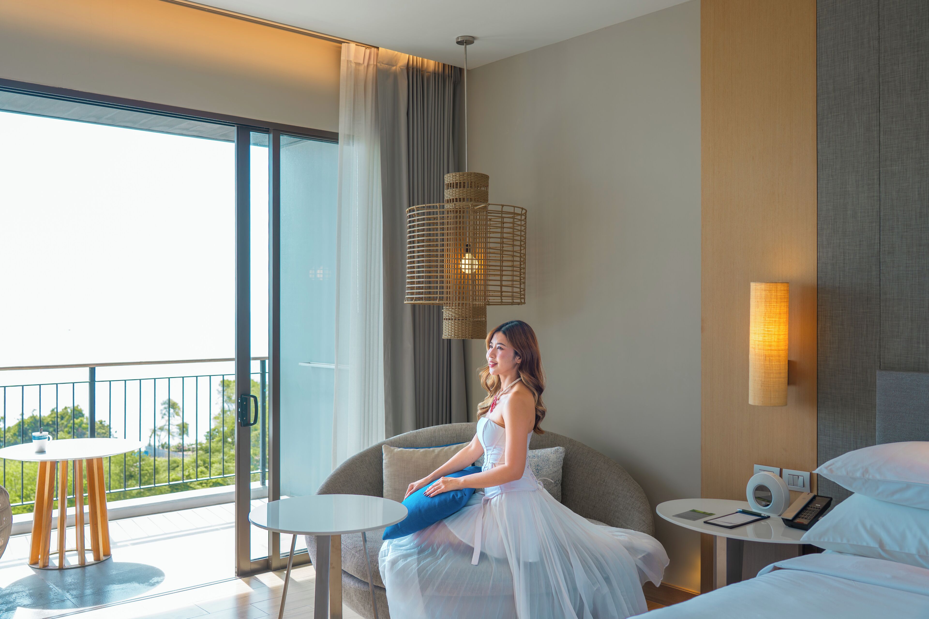Habitación de hotel con balcón, una cama, sofá, pequeña mesa y lámpara de pared.