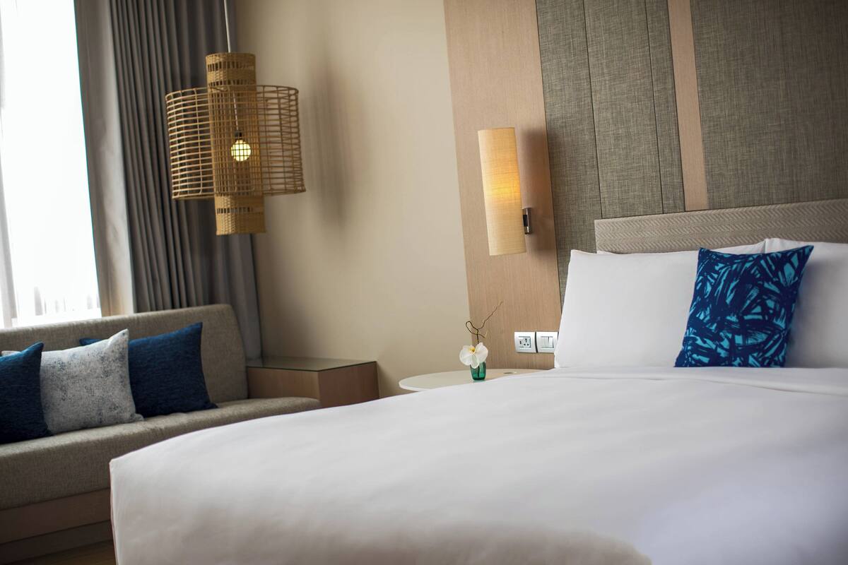 A hotel room with a large bed, a sofa, a nightstand, a wall-mounted lamp, and a vase with flowers.