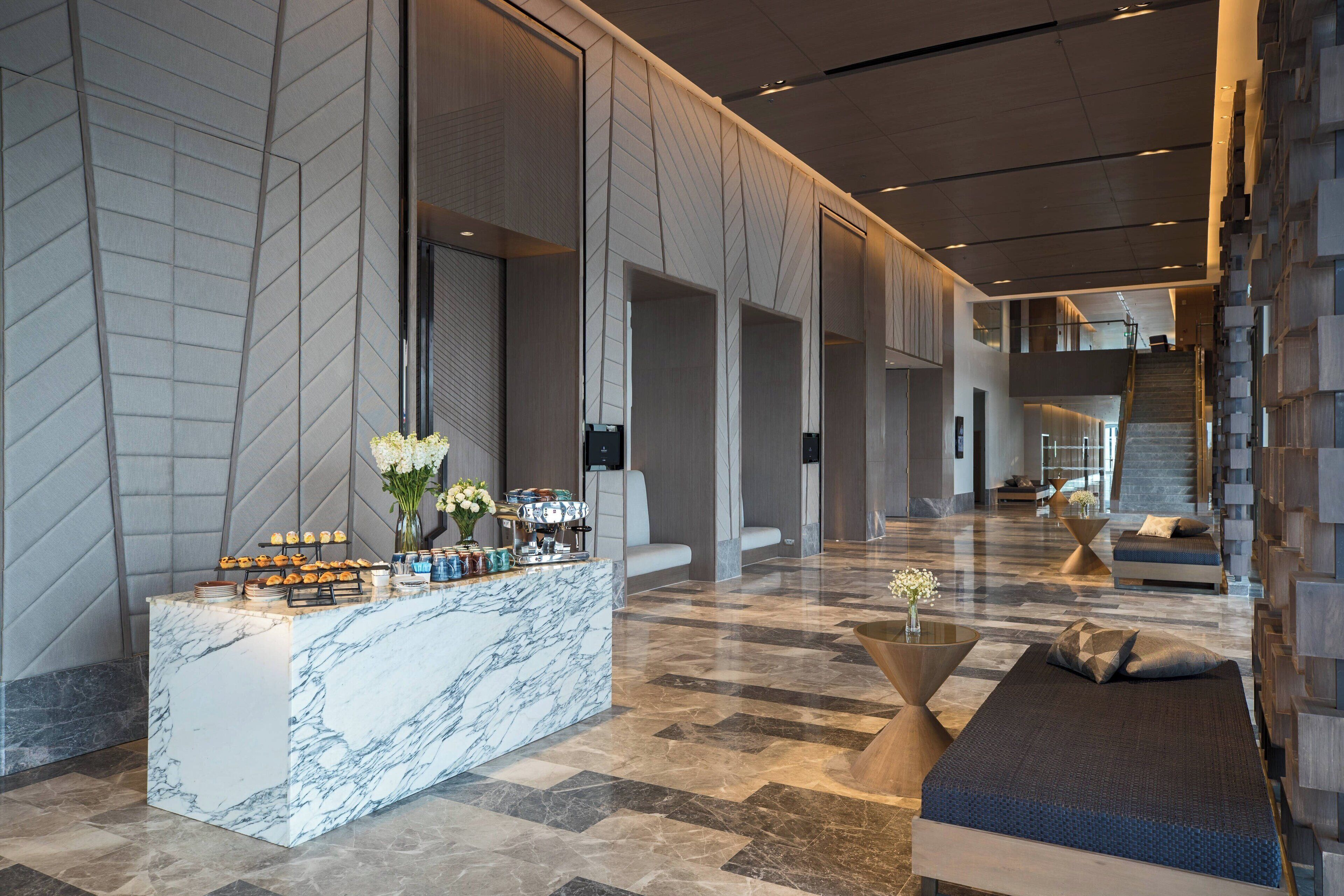 A modern lobby with a marble reception desk, seating areas, and a staircase.