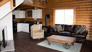 A cozy log cabin interior with a living room, a kitchen, and a staircase.