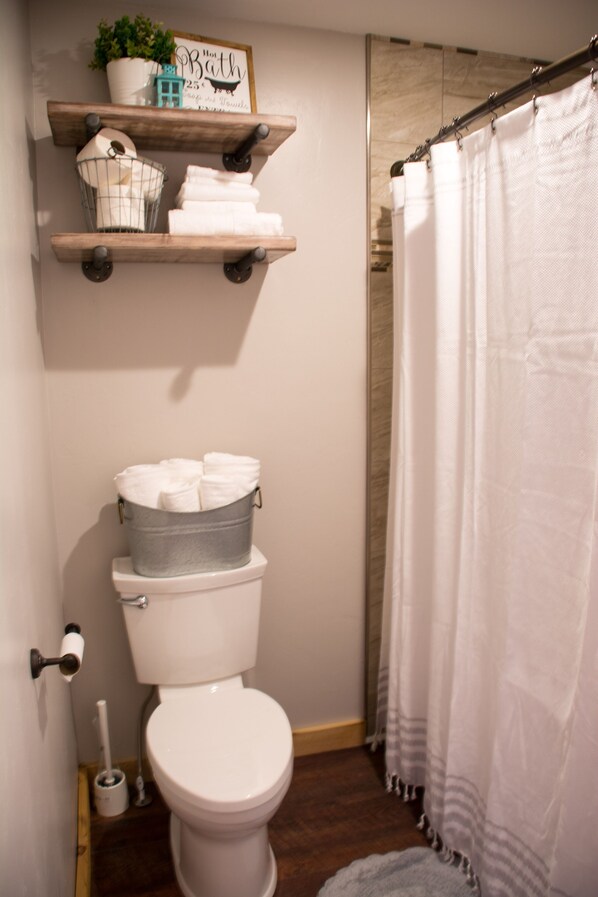 A bathroom with a toilet, a shelf with towels, a shower curtain, and a sign above the shelf. - Sit On The Porch And Enjoy The View Of The Tetons In South East Idaho (St.Anthony)