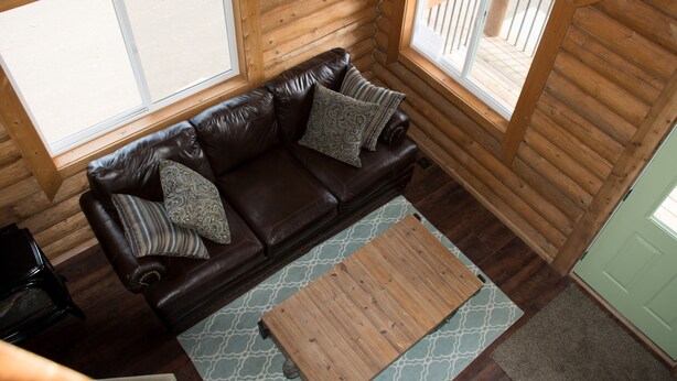 A cozy log cabin interior with a brown leather sofa, two patterned pillows, and a wooden coffee table.
