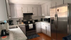 Una cocina con gabinetes blancos, un refrigerador de acero inoxidable, un microondas, una estufa y un lavamanos.