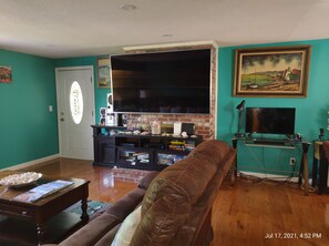 A living room with a large flat-screen TV, a brick fireplace, and a teal wall.