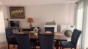 Un comedor con una mesa, sillas, un televisor, una lámpara y una lavadora.