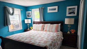 Un dormitorio con una cama, dos mesitas de noche, un ventanal con cortinas y una obra de arte en la pared.