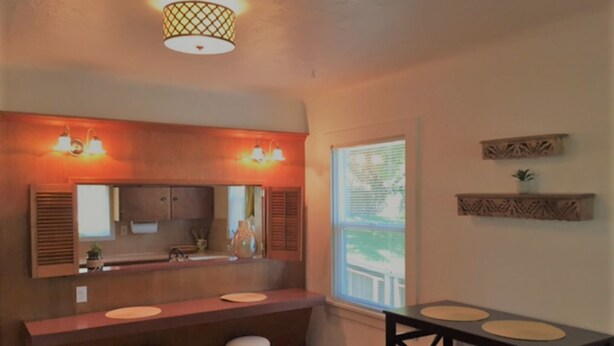 Una cocina con encimera de madera, tres taburetes, un ventanal con persianas y un estante decorativo.