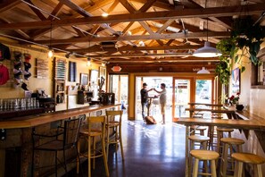 An interior with wooden beams, a bar area, stools, and a door leading outside.