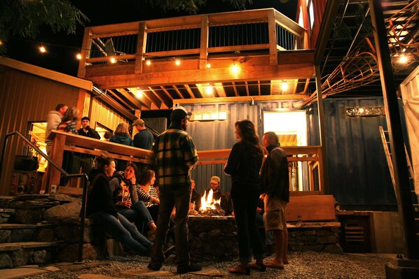 A rustic outdoor gathering area with a fire pit, wooden benches, and a covered seating area.