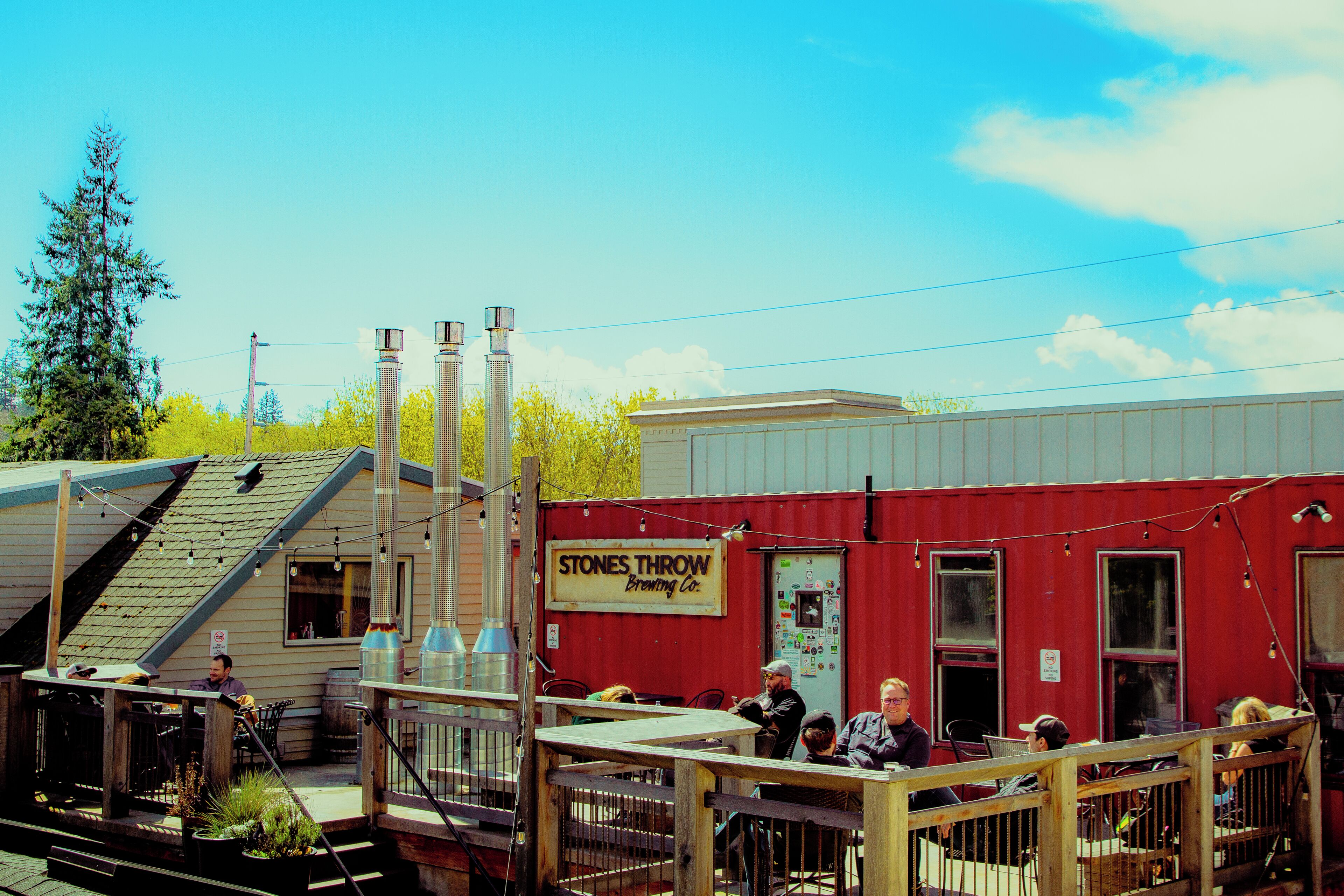 Un edificio rojo con un letrero que dice "Stones Throw Brewing Co." y un área de estar al aire libre cubierta.