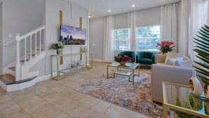 A modern living room with a staircase, a cityscape painting, and a green armchair. - Comfortable 4bdr w/private pool - No resort fees (Kissimmee)