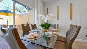 A dining area with a glass table, brown leather chairs, white plates, and a vase of white flowers. - Comfortable 4bdr w/private pool - No resort fees (Kissimmee)