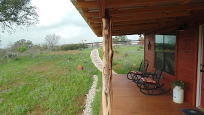 A wooden porch with two rocking chairs, a potted plant, and a view of a flower garden. - Texas T Bed and Breakfasts (Llano)
