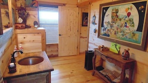A wooden cabin interior with a wooden sink, a door leading to another room, and a wall-mounted painting. - Texas T Bed and Breakfasts (Llano)