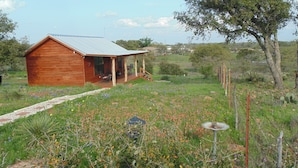 A wooden cabin with a metal roof, surrounded by a garden with various flowers and a small fountain. - Texas T Bed and Breakfasts (Llano)