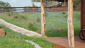 A garden with a wooden deck, a windmill in the background, and a fence. - Texas T Bed and Breakfasts (Llano)