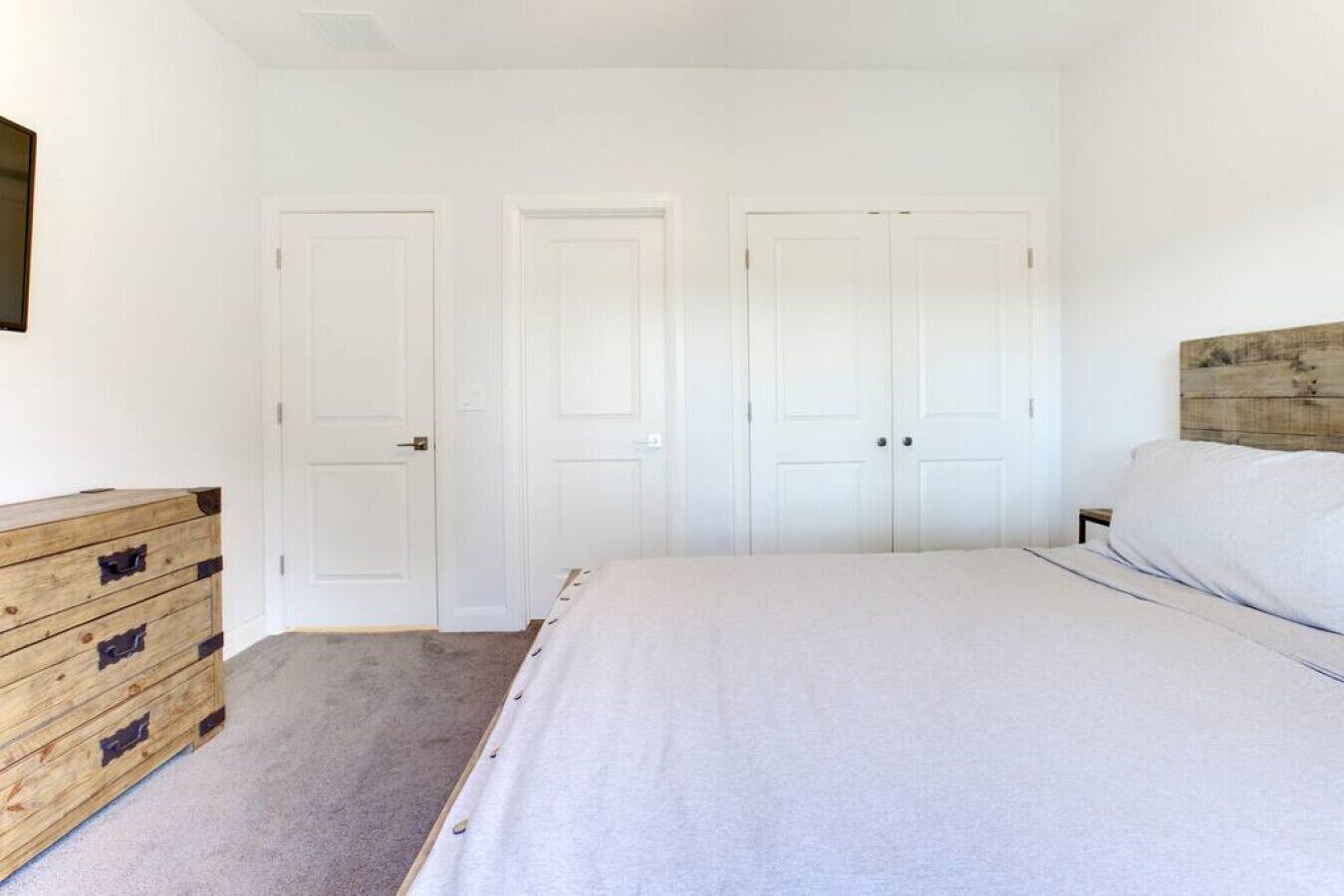 Un dormitorio con una cama, un aparador de madera y dos puertas blancas.