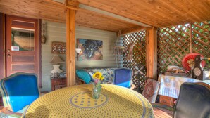 Een houten plafond, een ronde tafel met een gele tafelkleed en blauwe stoelen.