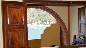 A wooden door with a view of a beach and houses through an arched window. - Oceanfront Yelapa (yelapa)