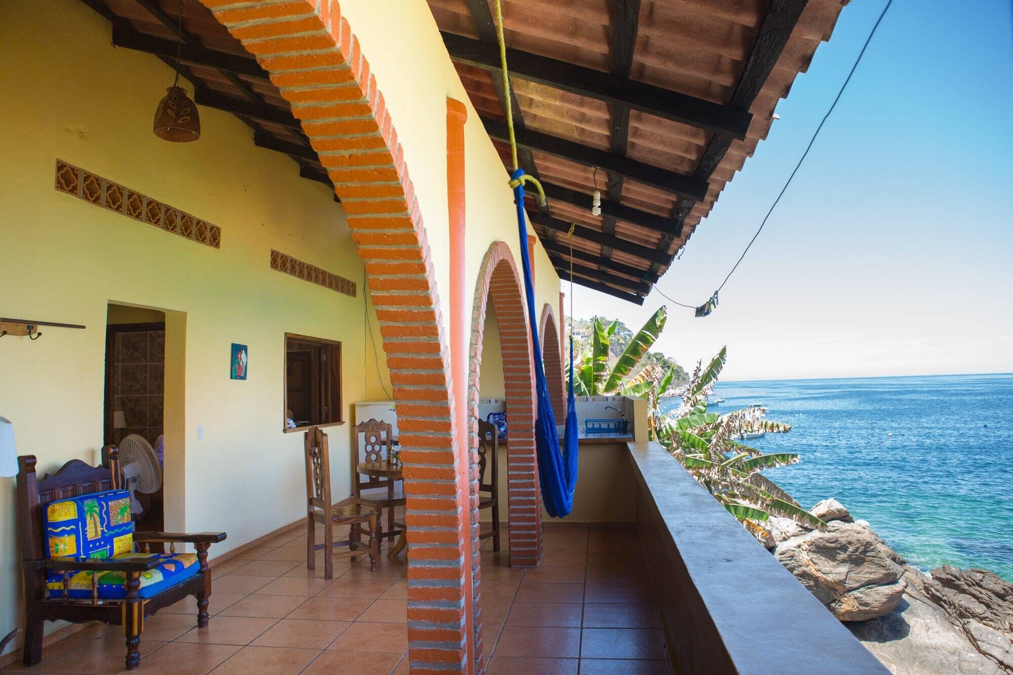 A coastal property with a covered patio, a dining area with chairs, and a view of the sea.