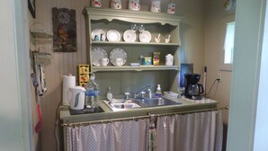 Une petite cuisine équipée d’un évier, d’une machine à café et d’une étagère où sont disposés des objets décoratifs.