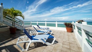 A terrace with sun loungers, potted plants, and a view of the sea. - Beach House Condos: Beachfront Ocean House - 7mile Beach Jamaica (Negril)