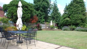 An outdoor patio with a table and chairs, surrounded by a well-maintained lawn and various trees.