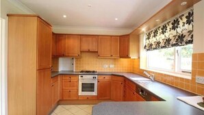 A kitchen with wooden cabinets, a stove, and a window with a floral curtain.