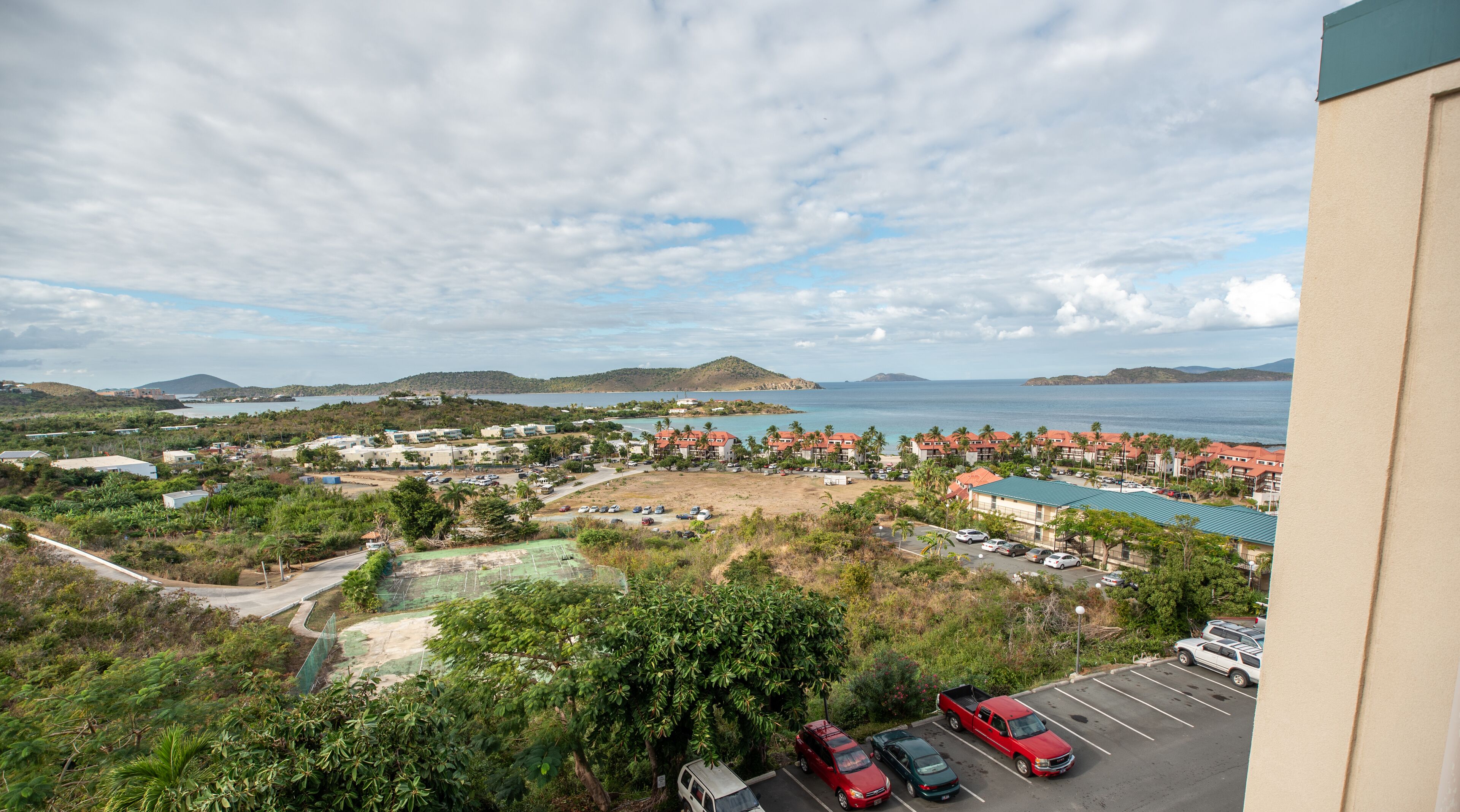 A coastal resort with multiple buildings, a parking lot, and a view of the sea and hills.