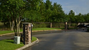 A gated driveway with a stone pillar, a metal fence, and a parked car. - Baton Rouge Condo With Resort Atmosphere With Custom Decor, Sleeps 2 (Baton Rouge)