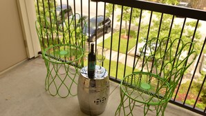 A balcony with two green wire chairs and a metal container with a bottle and glass. - Baton Rouge Condo With Resort Atmosphere With Custom Decor, Sleeps 2 (Baton Rouge)