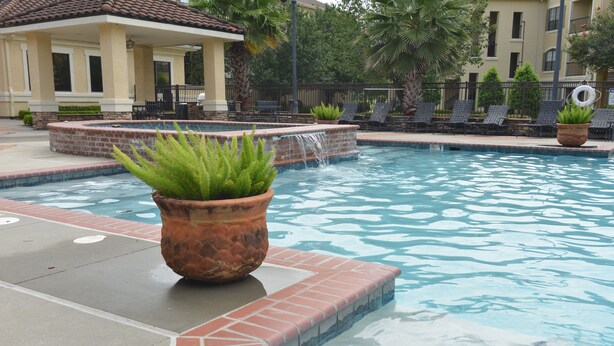A swimming pool with a brick border, a waterfall feature, and lounge chairs. - Baton Rouge Condo With Resort Atmosphere With Custom Decor, Sleeps 2 (Baton Rouge)