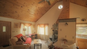 A cozy living room with a wooden ceiling, a sofa, a coffee table, and a dining area with a table and chairs. - The Cedar House Is Uniquely Set In The Forest Surrounded By Decks And Porches. (McGrath)