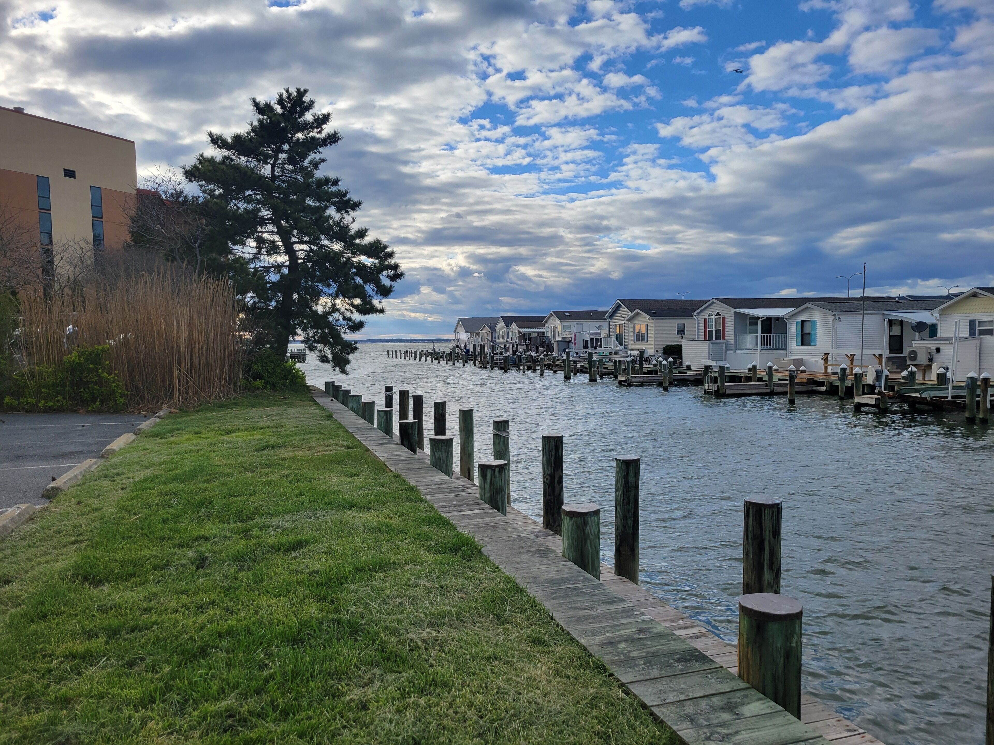 A waterfront property with a grassy walkway, wooden docks, and row houses.