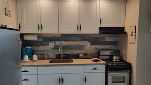 A compact kitchen with white cabinets, a stainless steel sink, a kettle, and a microwave. - Romantic Beach Getaway For 2 In Ocean City MD (Ocean City)