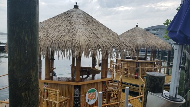 A wooden deck with thatched-roof structures, likely a bar or lounge area, overlooking a body of water. - Romantic Beach Getaway For 2 In Ocean City MD (Ocean City)