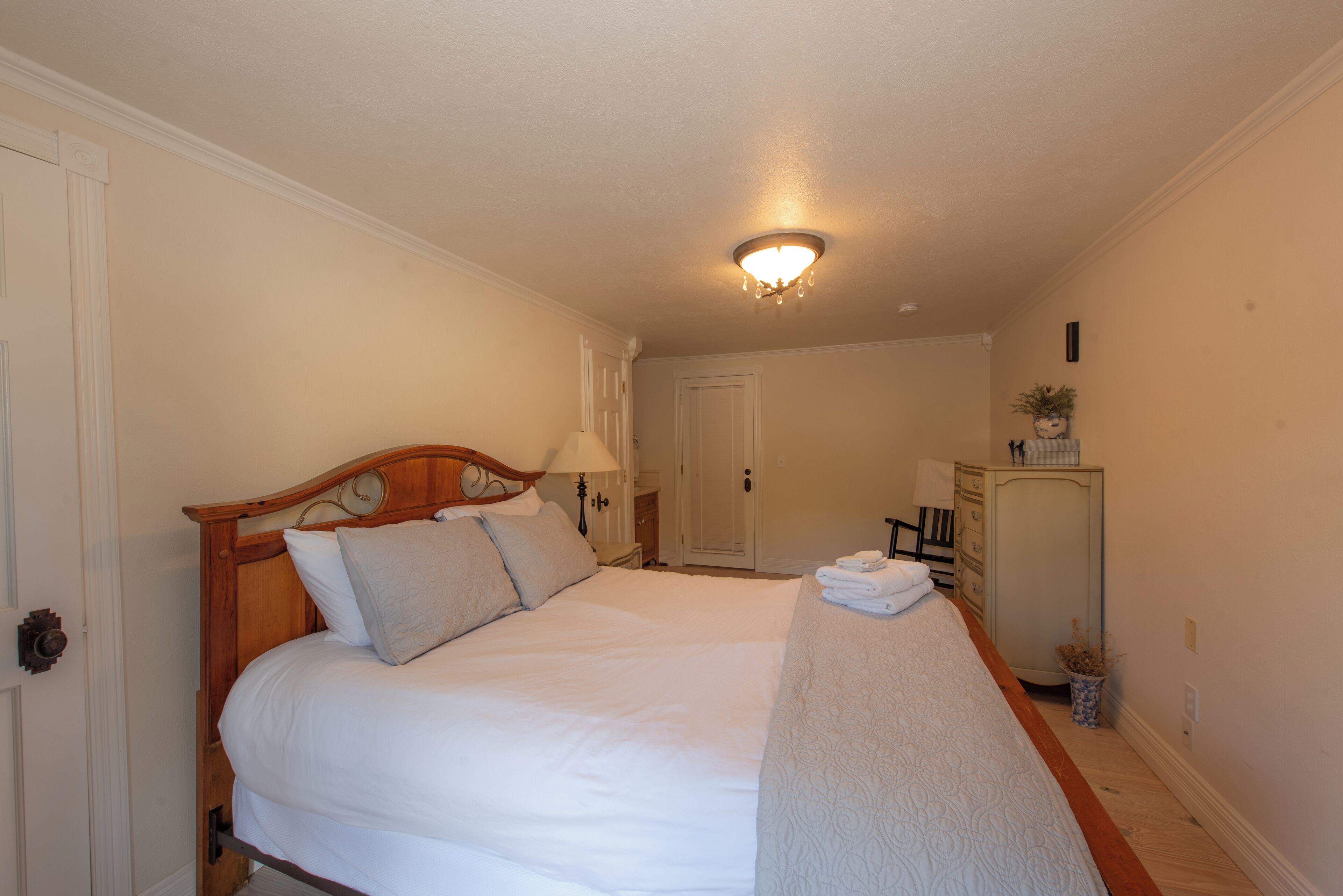 A neatly made bed with a wooden headboard, a bedside lamp, and a small table with a folded towel.