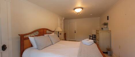A neatly made bed with a wooden headboard, a bedside lamp, and a small table with a folded towel.