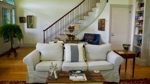 Ein Wohnzimmer mit einem weißen Sofa, einem Couchtisch mit Zeitschriften, einer Treppe und einem Bücherregal.
