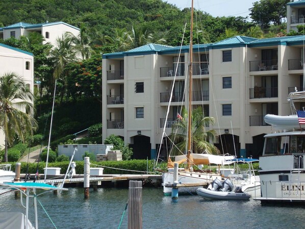 Un puerto deportivo con barcos amarrados, un edificio con balcones y exuberante vegetación al fondo.