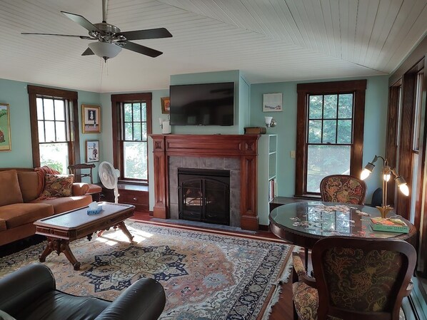A living room with a fireplace, a ceiling fan, a television, and a dining area with chairs.
