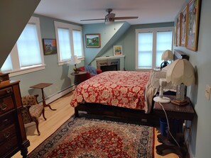 A bedroom with a bed, a desk, a chair, a rug, a dog, and a ceiling fan.