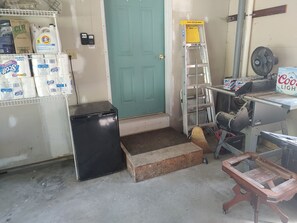 A room with a green door, a black trash bin, a broom, a ladder, and a Coors Light beer box. - Lakefront Vacation Home on Lake Elmore (Elmore)